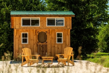 Exterior of cabin with two muskoka chairs and nature surrounding