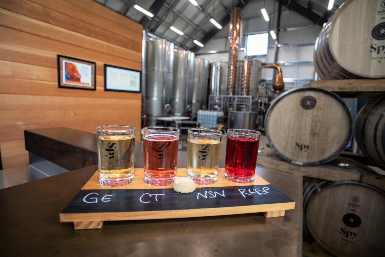 Four ciders of various colours on a wooden serving tray.