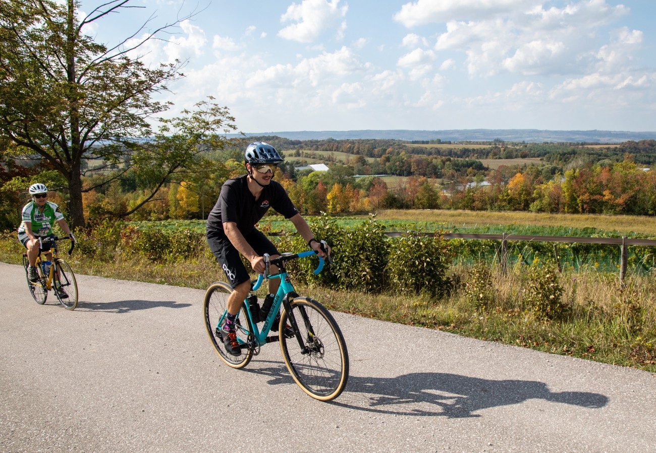 Two cyclists ride up a hill in a rural area.