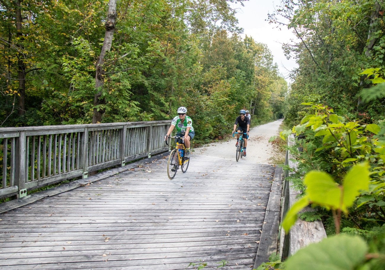 Three cyclists ride onto a wooden bridge.