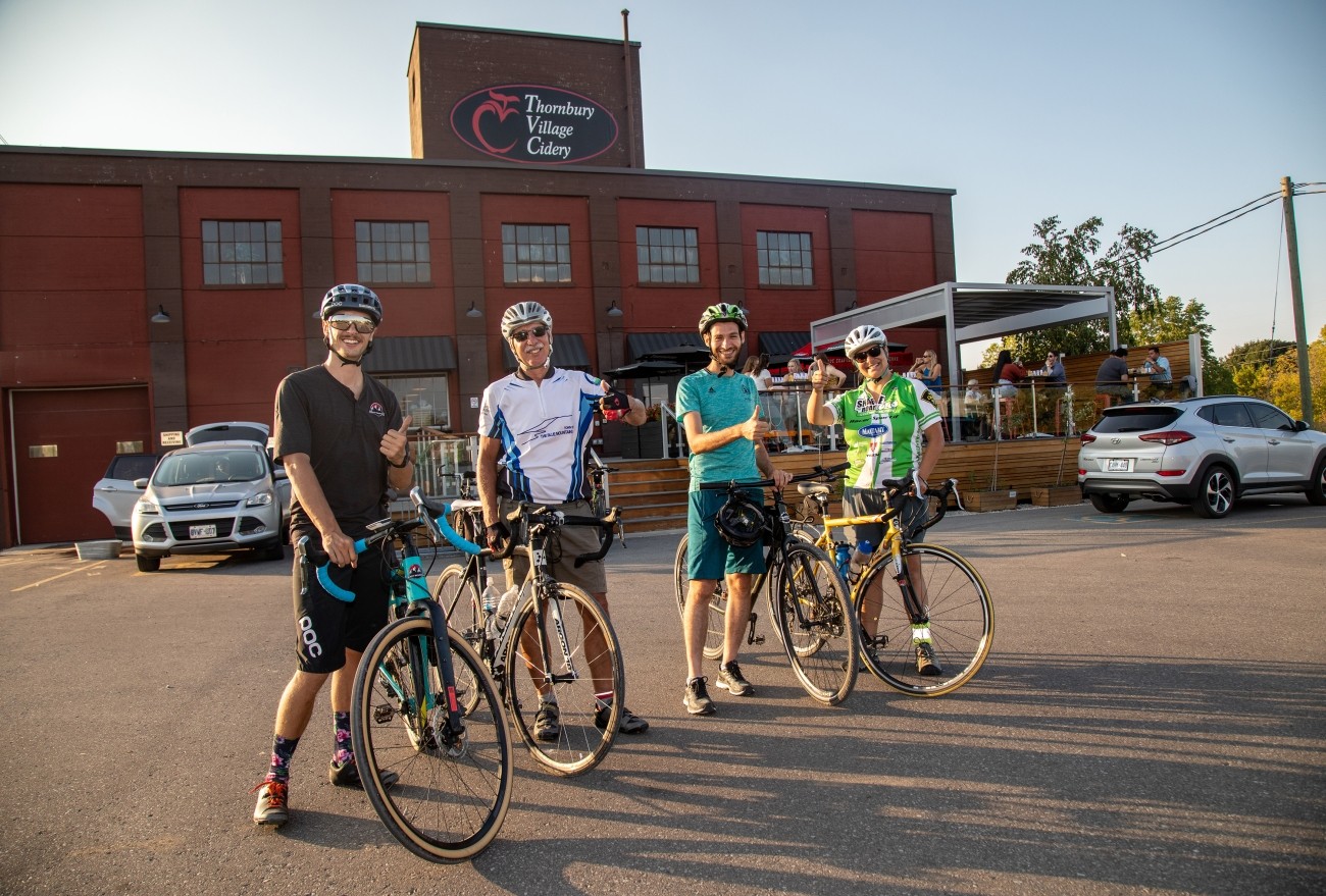 Four cyclists pose with their bicycles in front of a business.