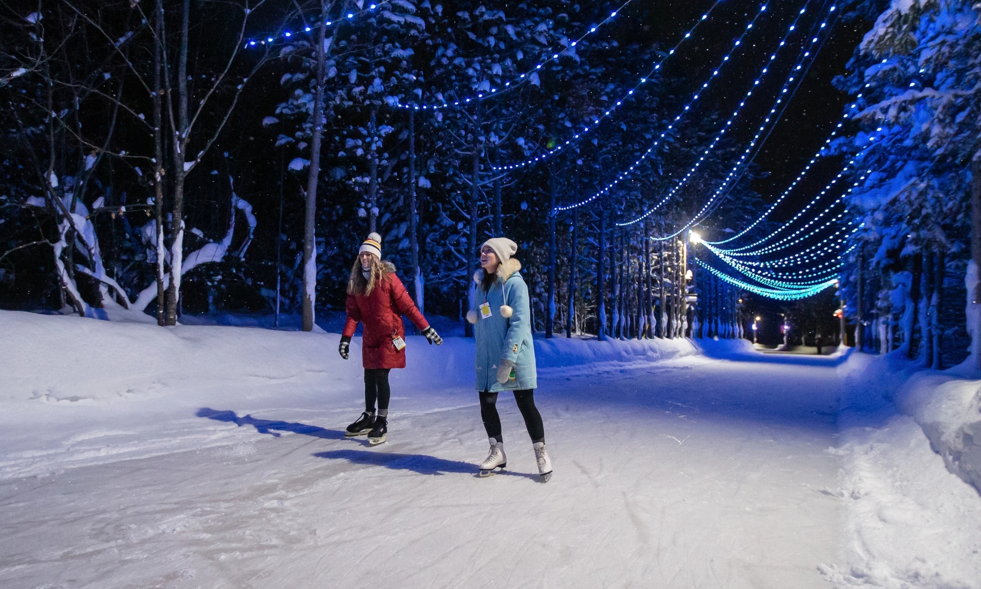 Two skaters on an outdoor skating trail lit up by blue string lights.