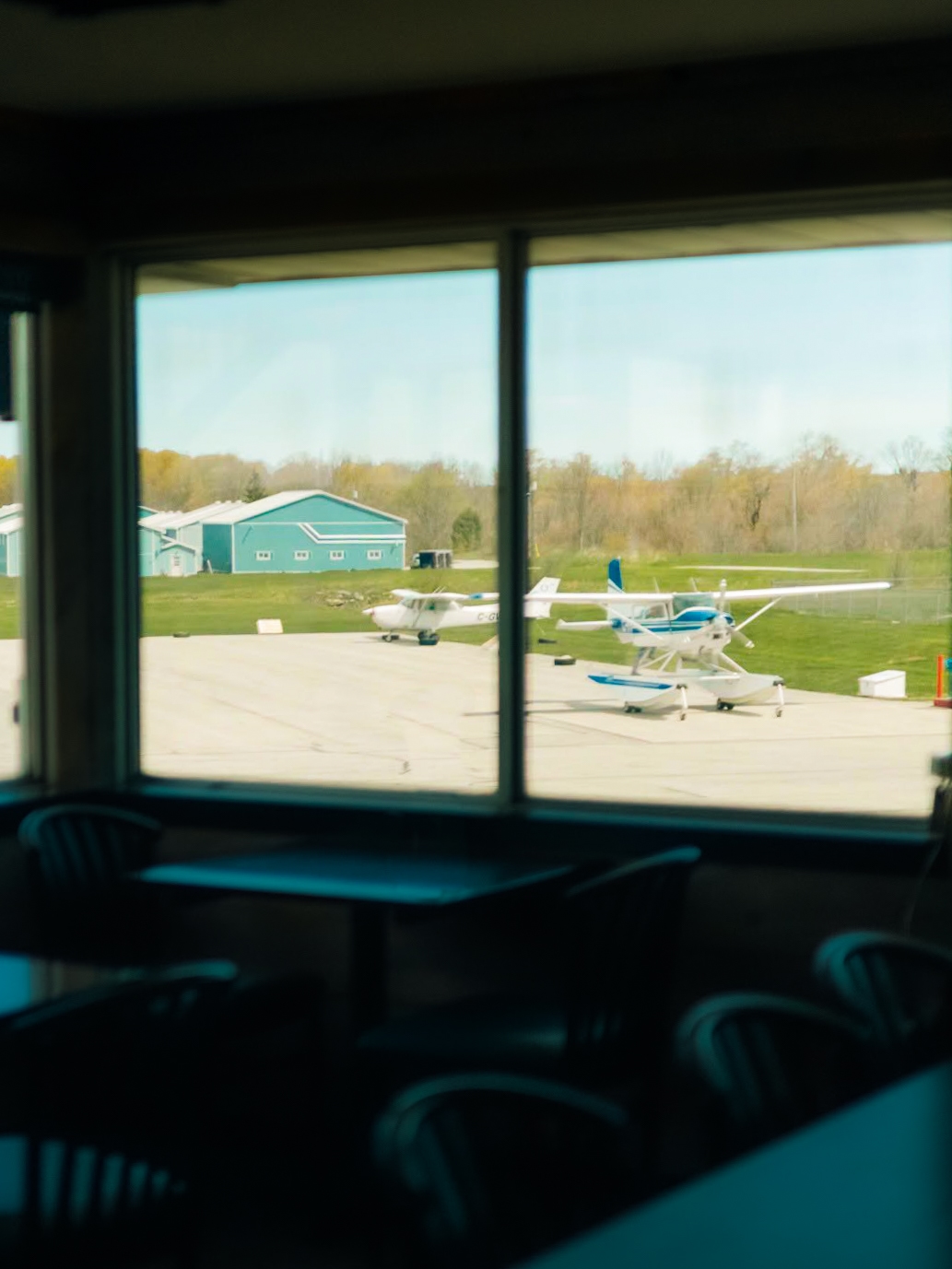 Looking out a restaurant window, two small airplanes are parked on tarmac.