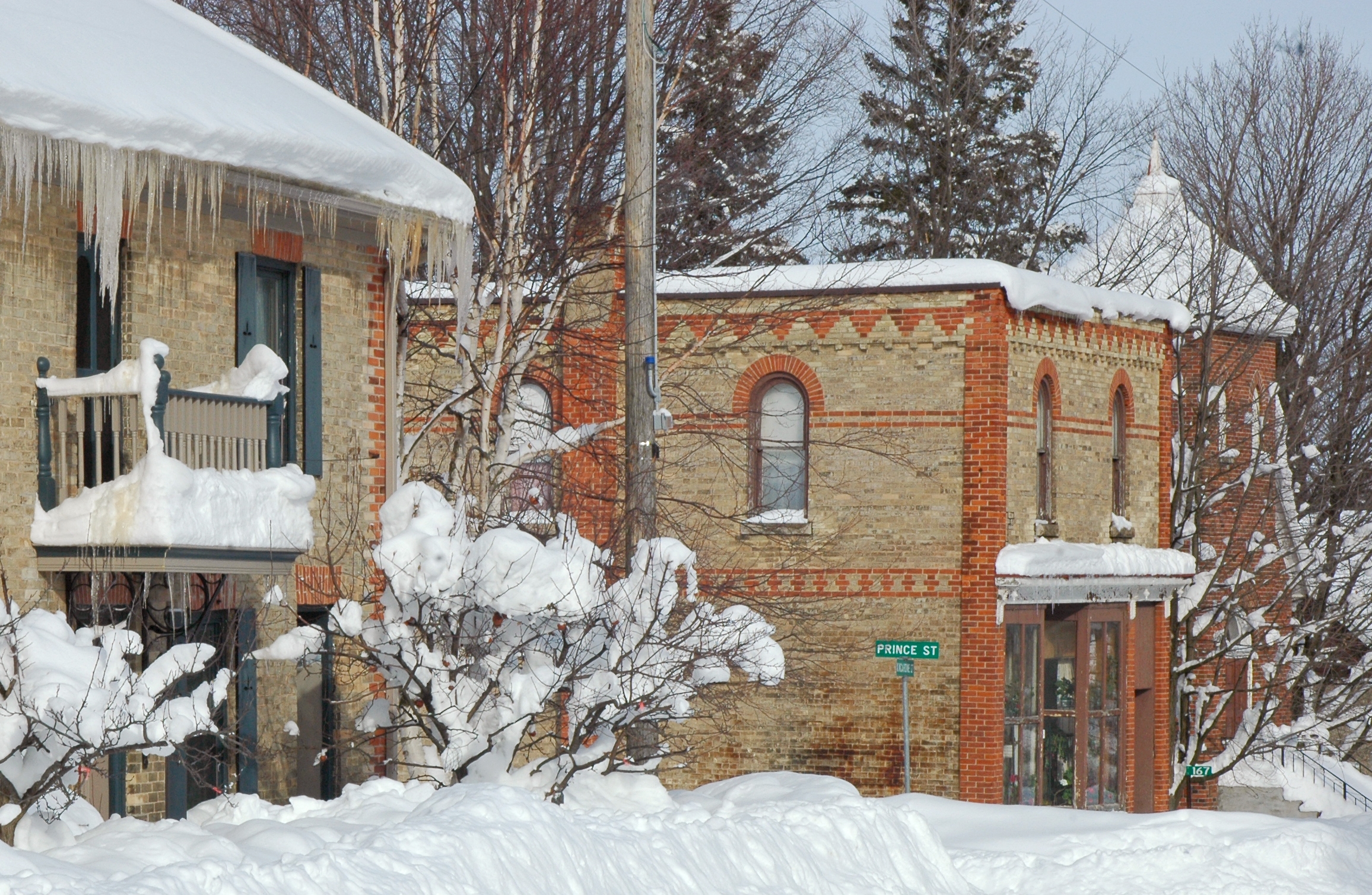 Snow-covered brick buildings on a quiet street with icicles hanging from roofs.