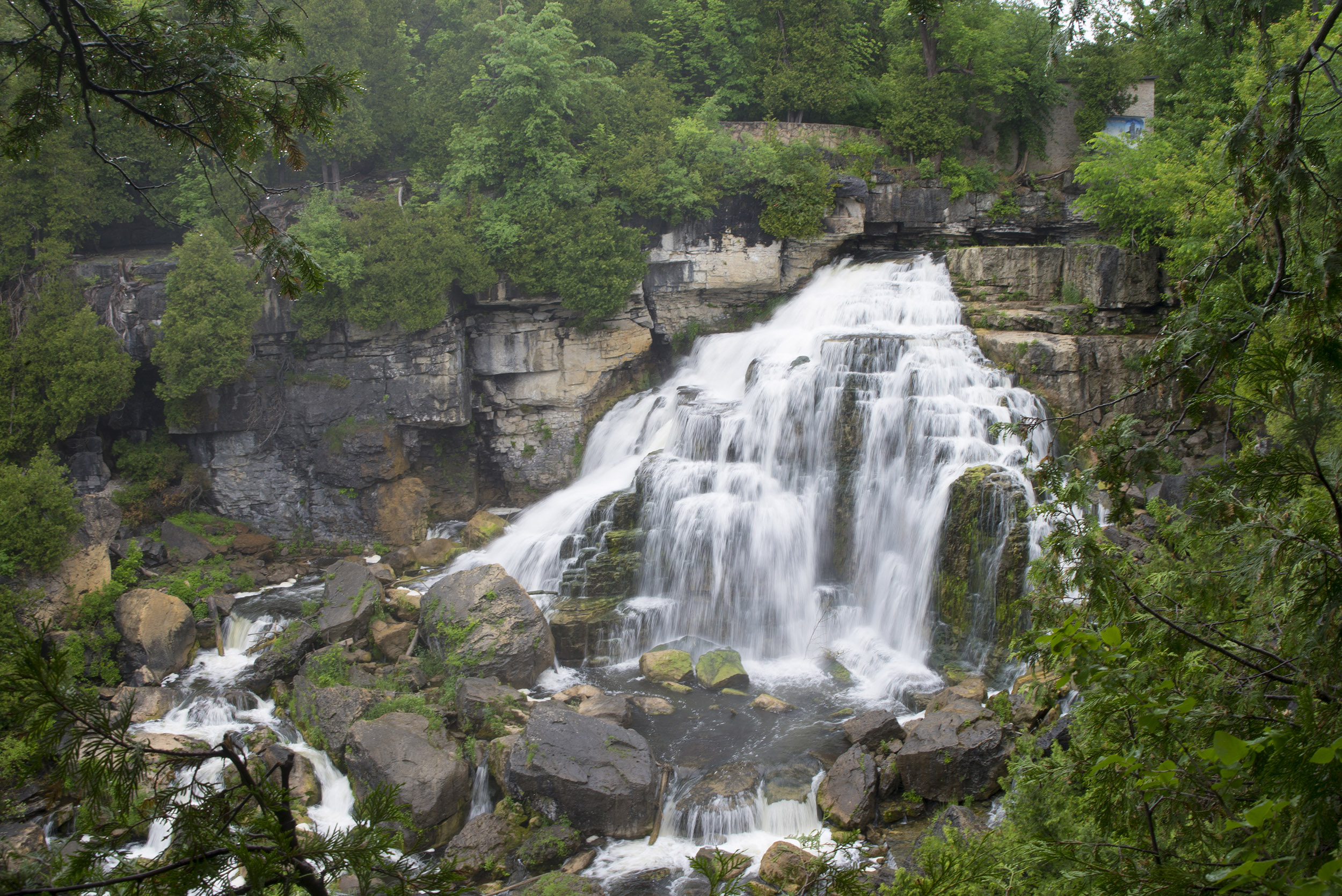 Large tiered waterfall cascading over rocky cliffs surrounded by dense green trees.