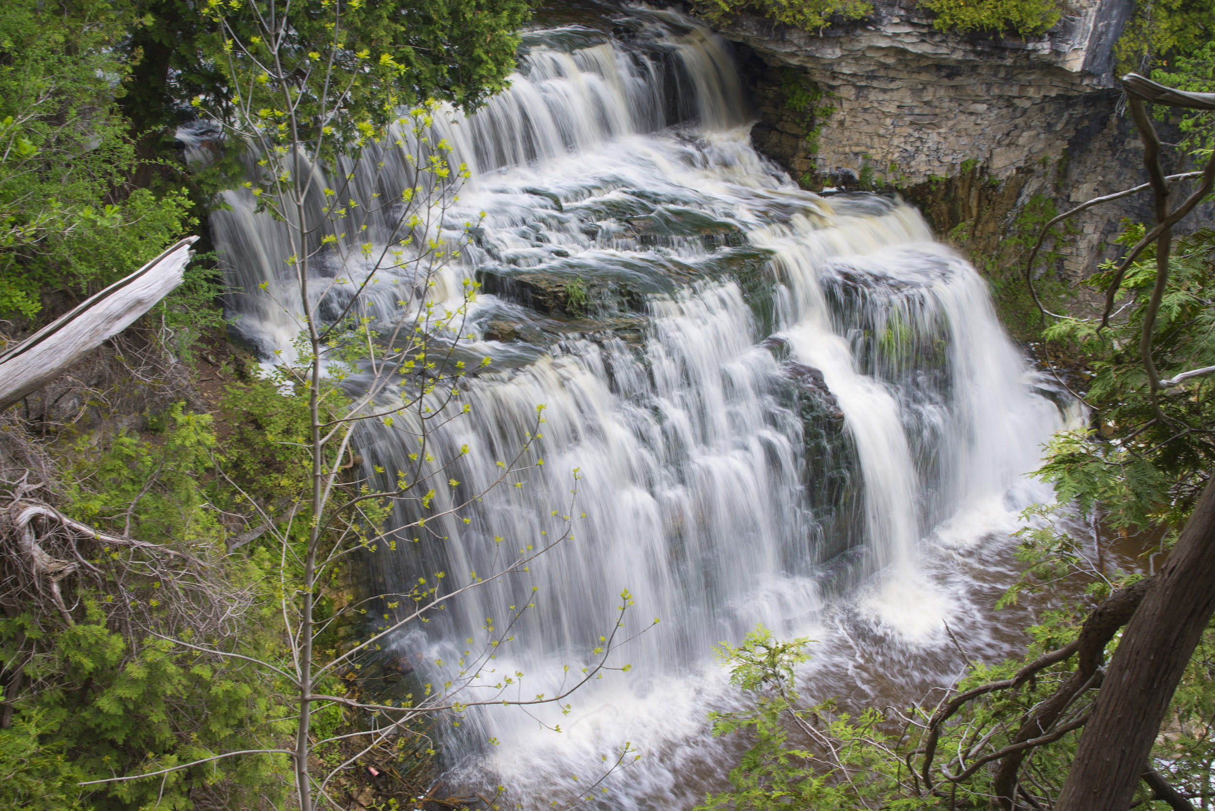 Here’s brief, accessible alt text: Alt text: “Multi-tiered waterfall flowing over rocky ledges and surrounded by green forest.