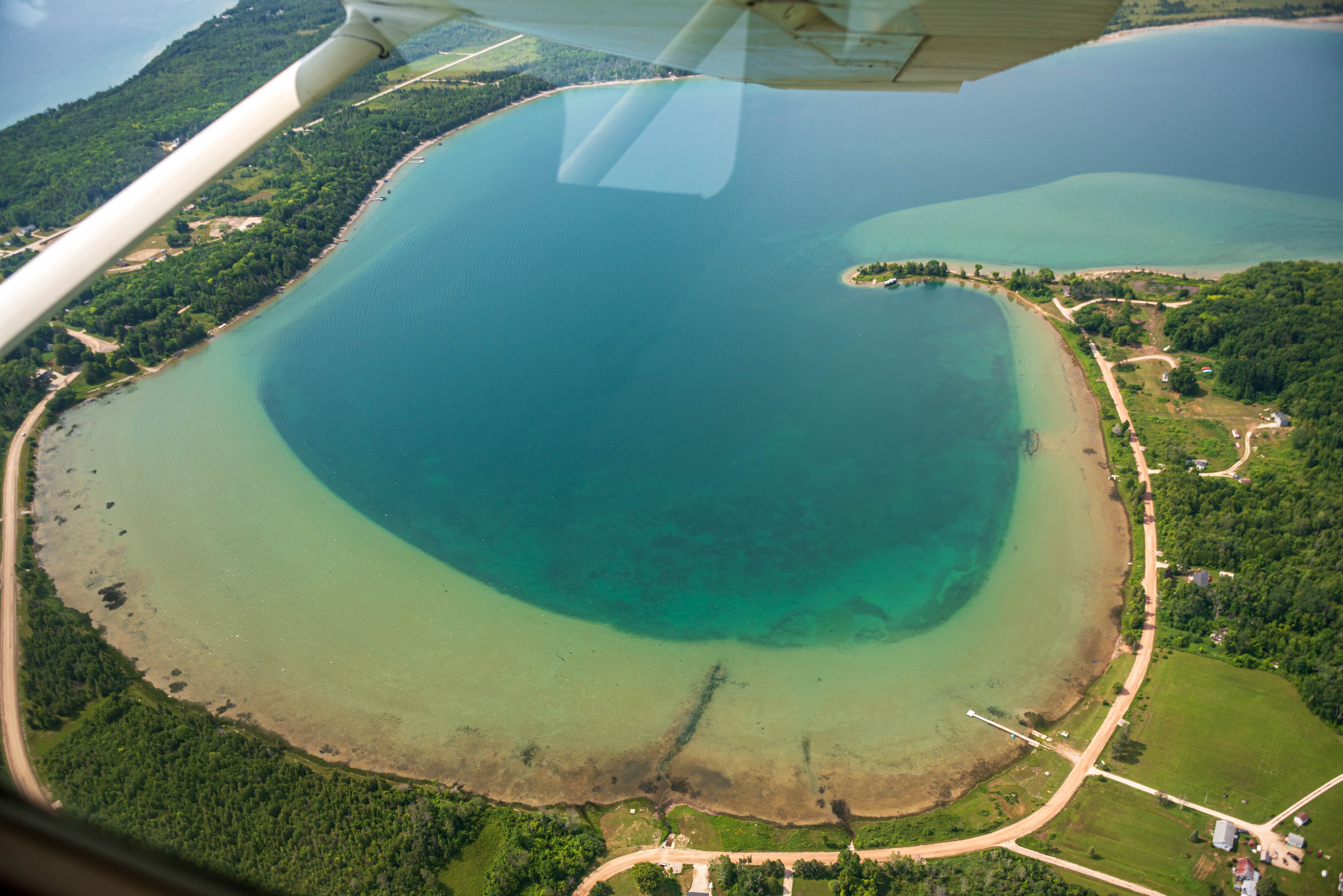 Aerial view of a small cove with a road running along beside. A wooden shipwreck is visible near the shore.