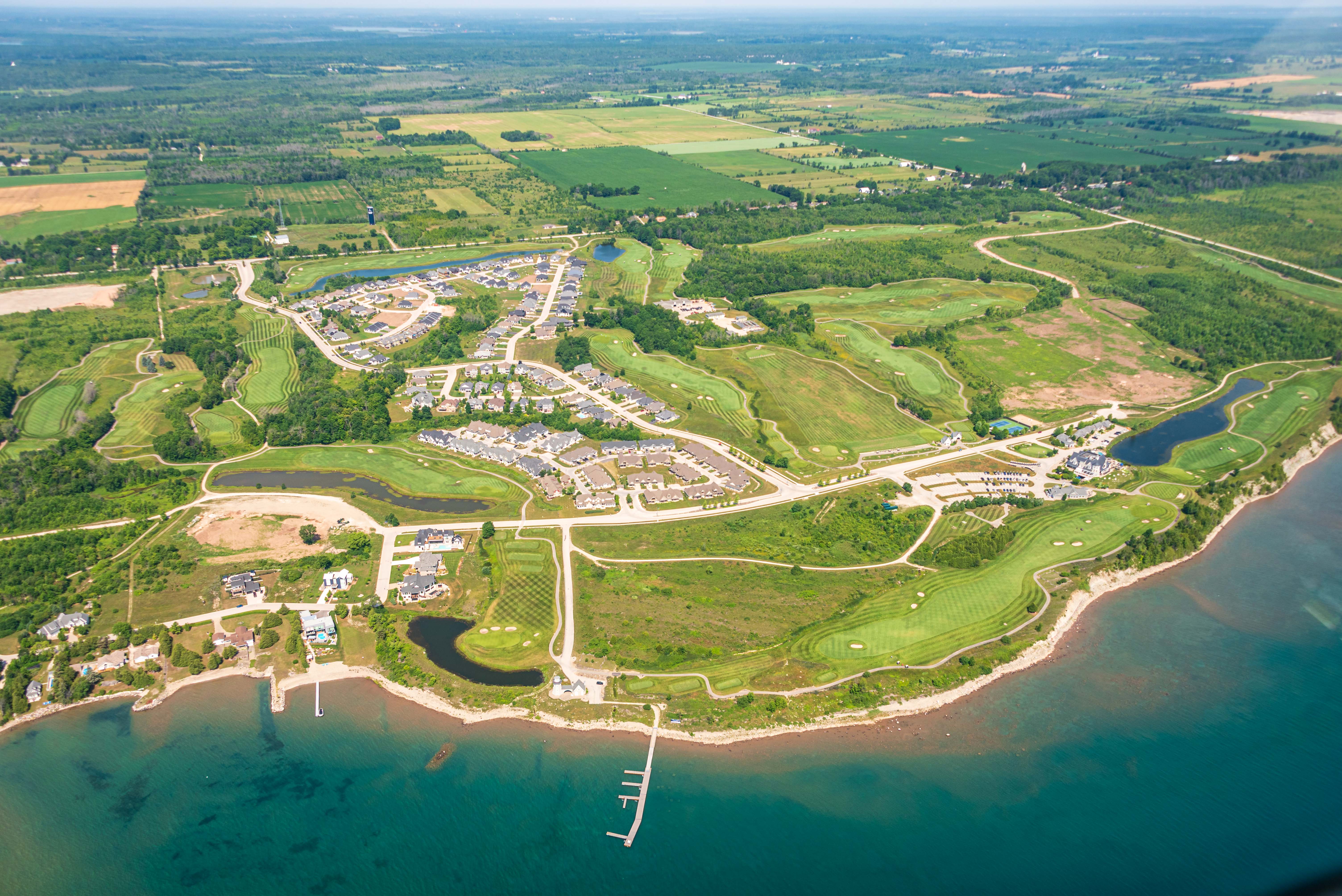 Aerial view of a golf course and community located immediately beside the shore of a scenic bay.