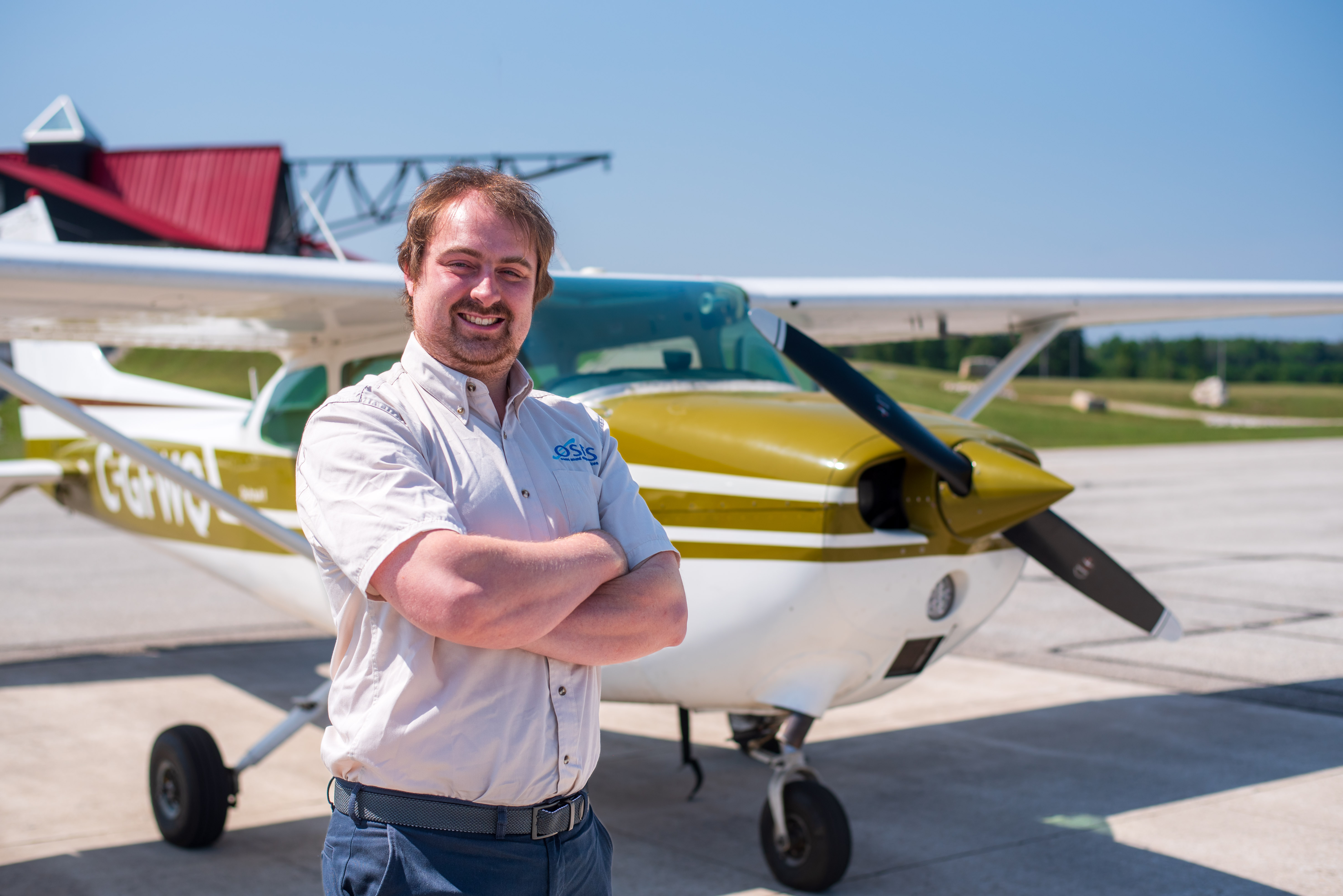 A pilot stands with folded arms beside a small aircraft.