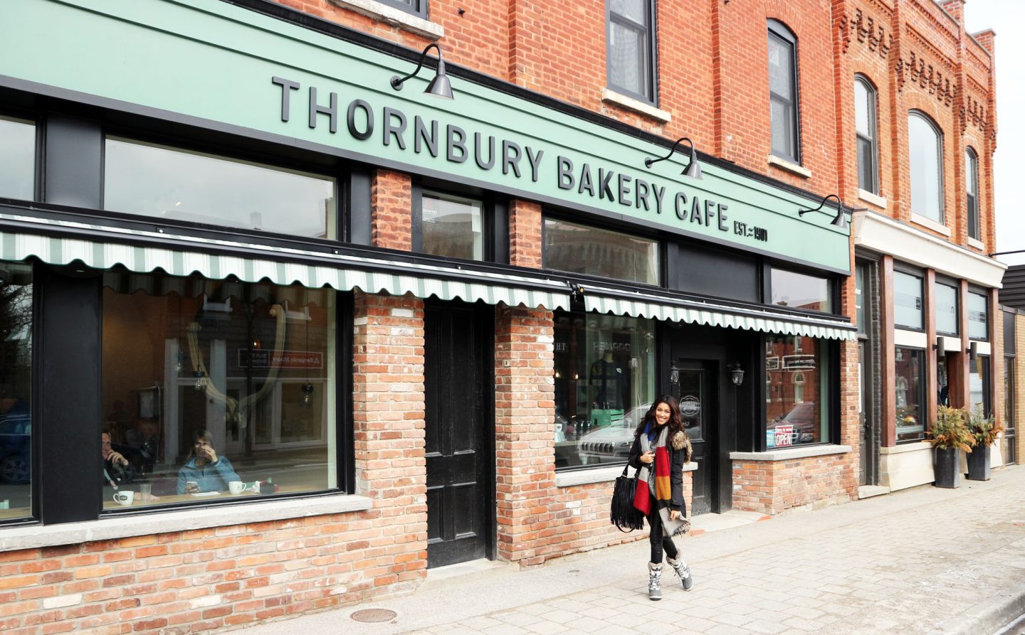 A person standing in front of a brick store. Sign reads THORNBURY BAKERY CAFE.