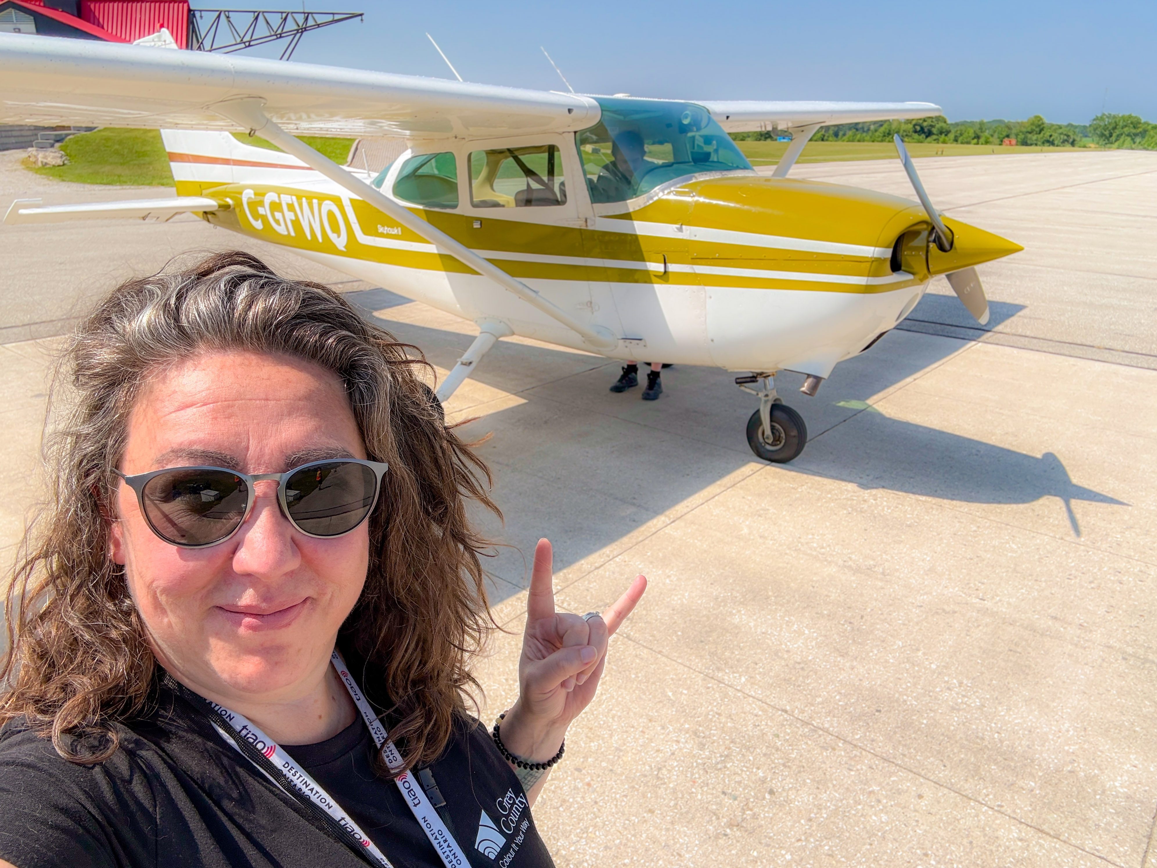 A person wearing sunglasses poses for a selfie beside a small aircraft.