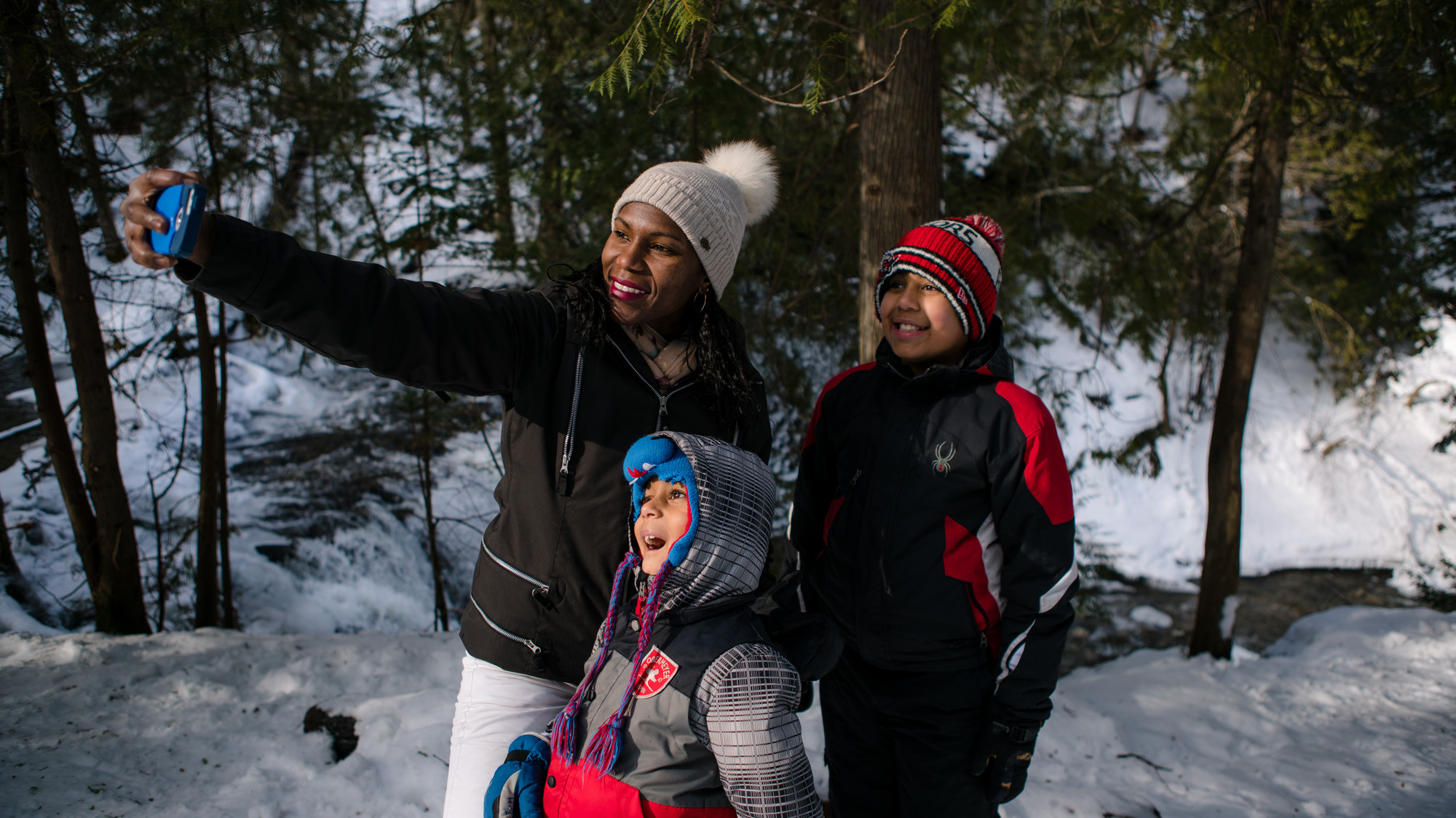 An adult and two children pose for a selfie in a snowy forest.
