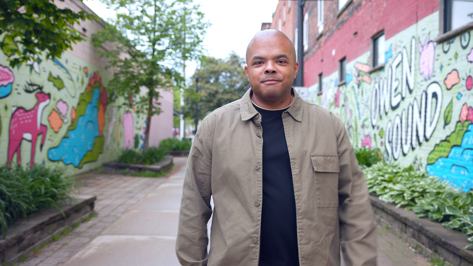 A man wearing a tan shirt stands in an alley.