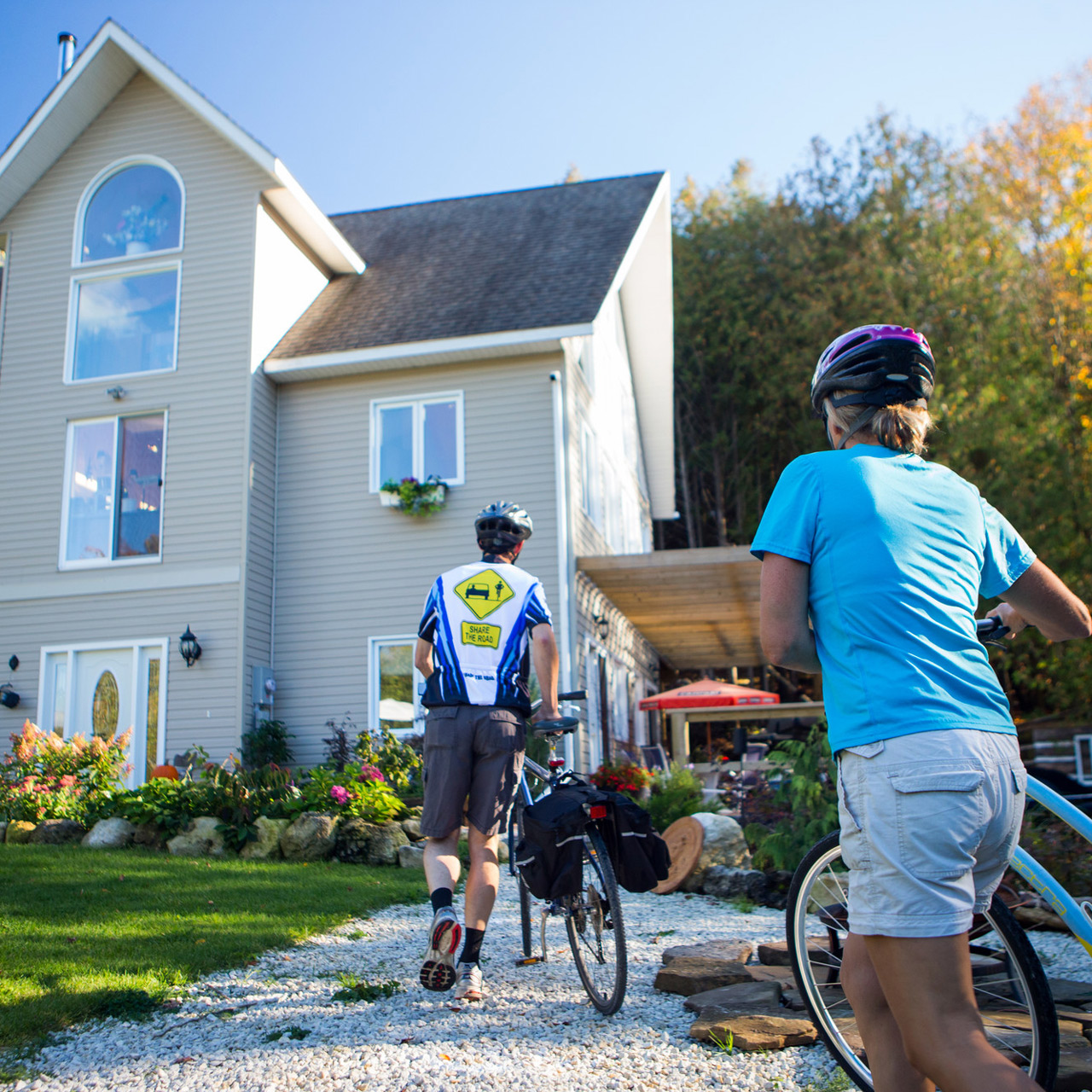 Two cyclists arrive by bike at a cozy country guesthouse surrounded by trees and gardens.