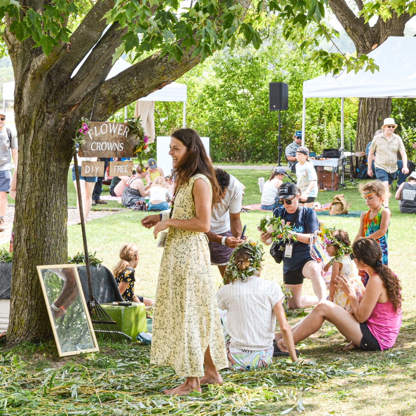 An outdoor activity held under a tree. A group of people assemble flower crowns.