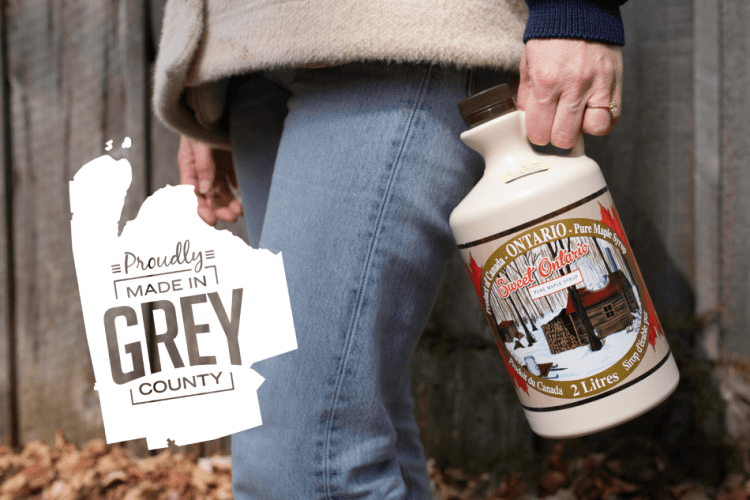 Close shot of a hand holding a two litre jug of maple syrup.