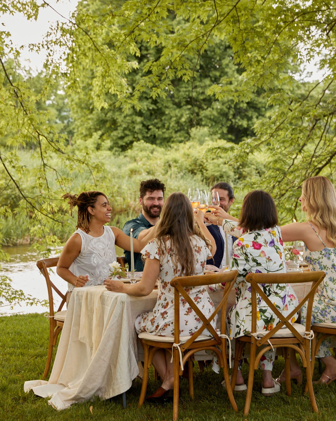 At an outdoor dining table, smiling friends raise a toast.