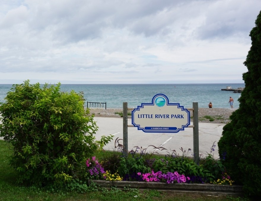 Little River Beach Park sign in front of bushes with a beach view