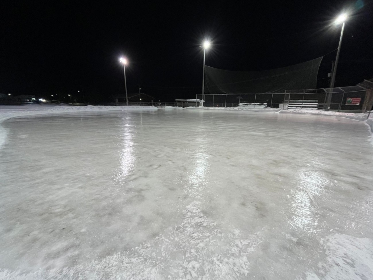 An outdoor rink at night, lit up by lightpoles.