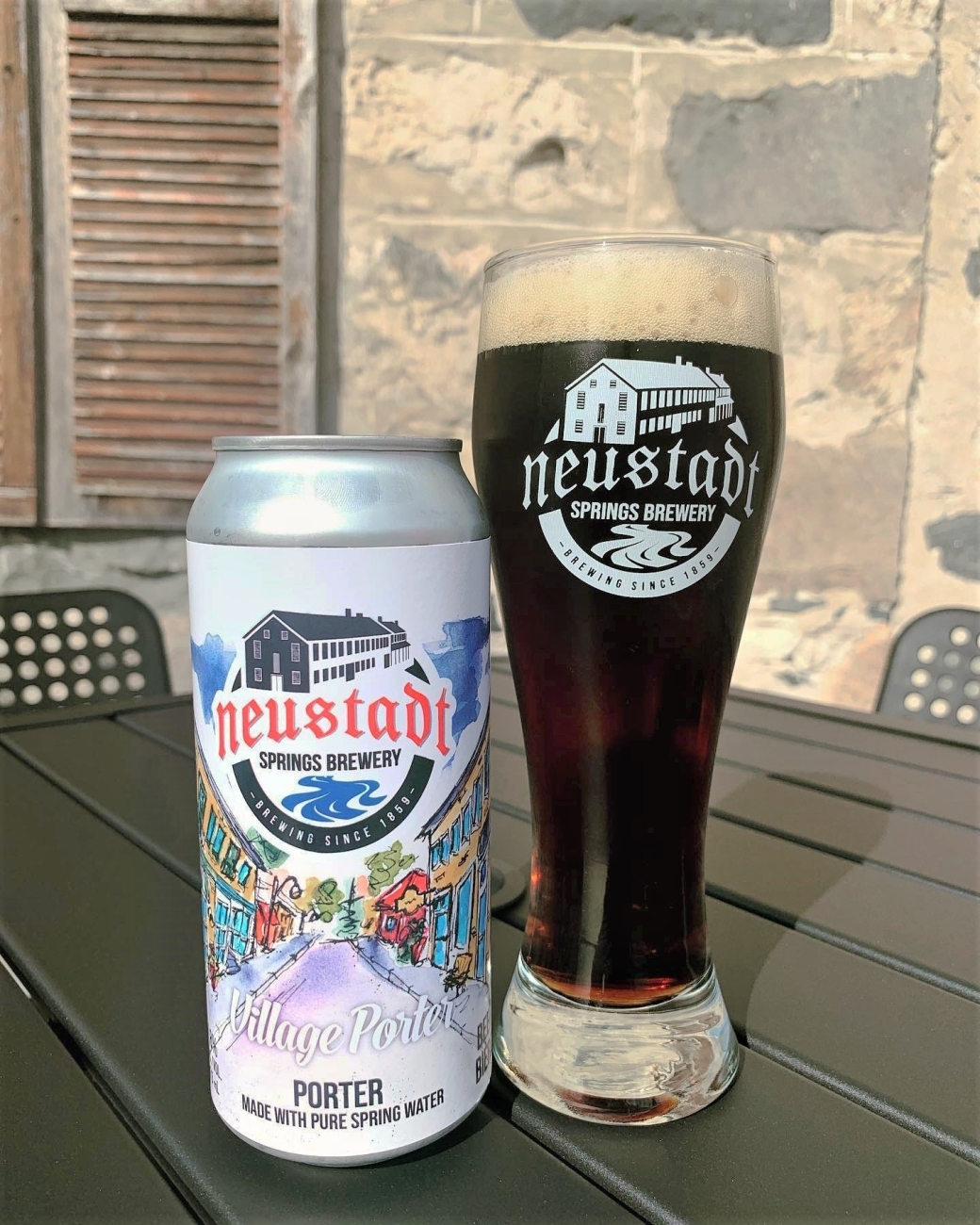 A can of beer beside a tall glass of dark brown beer.