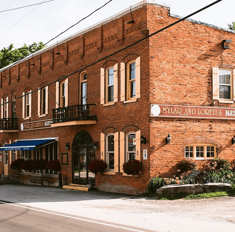 Historic brick restaurant building with cream shutters and flower planters out front.
