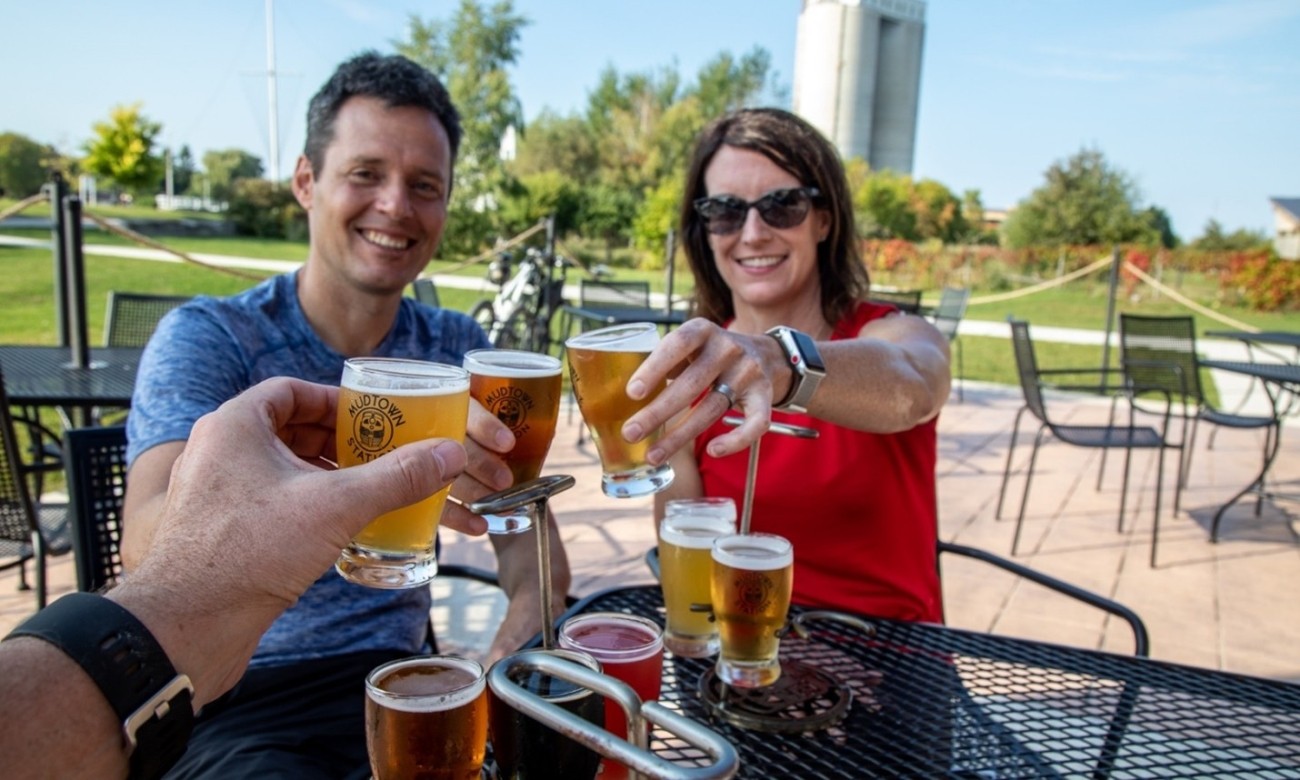 Three people raise and clink small glasses of beer while seated outdoors.
