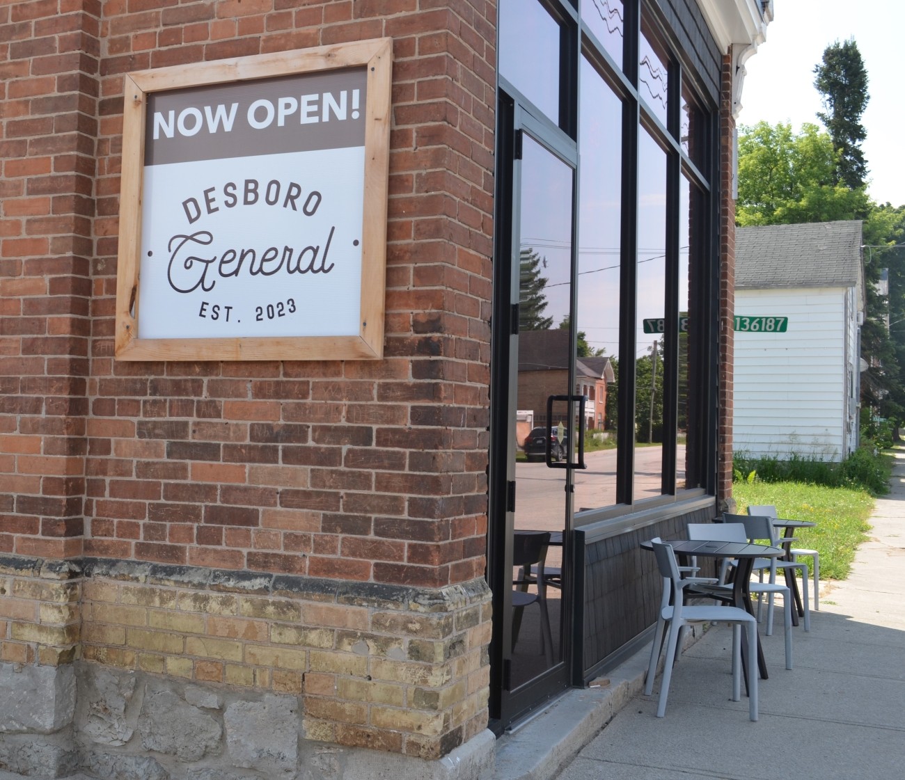 Wooden framed sign on a brick wall declares Now open! Desboro General Store.