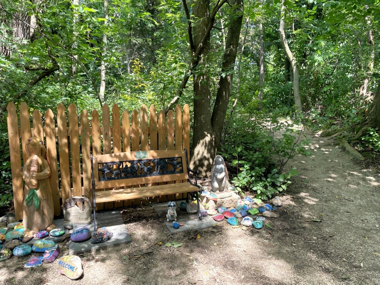 Many painted stones sit beside a bench beside a forest trail.