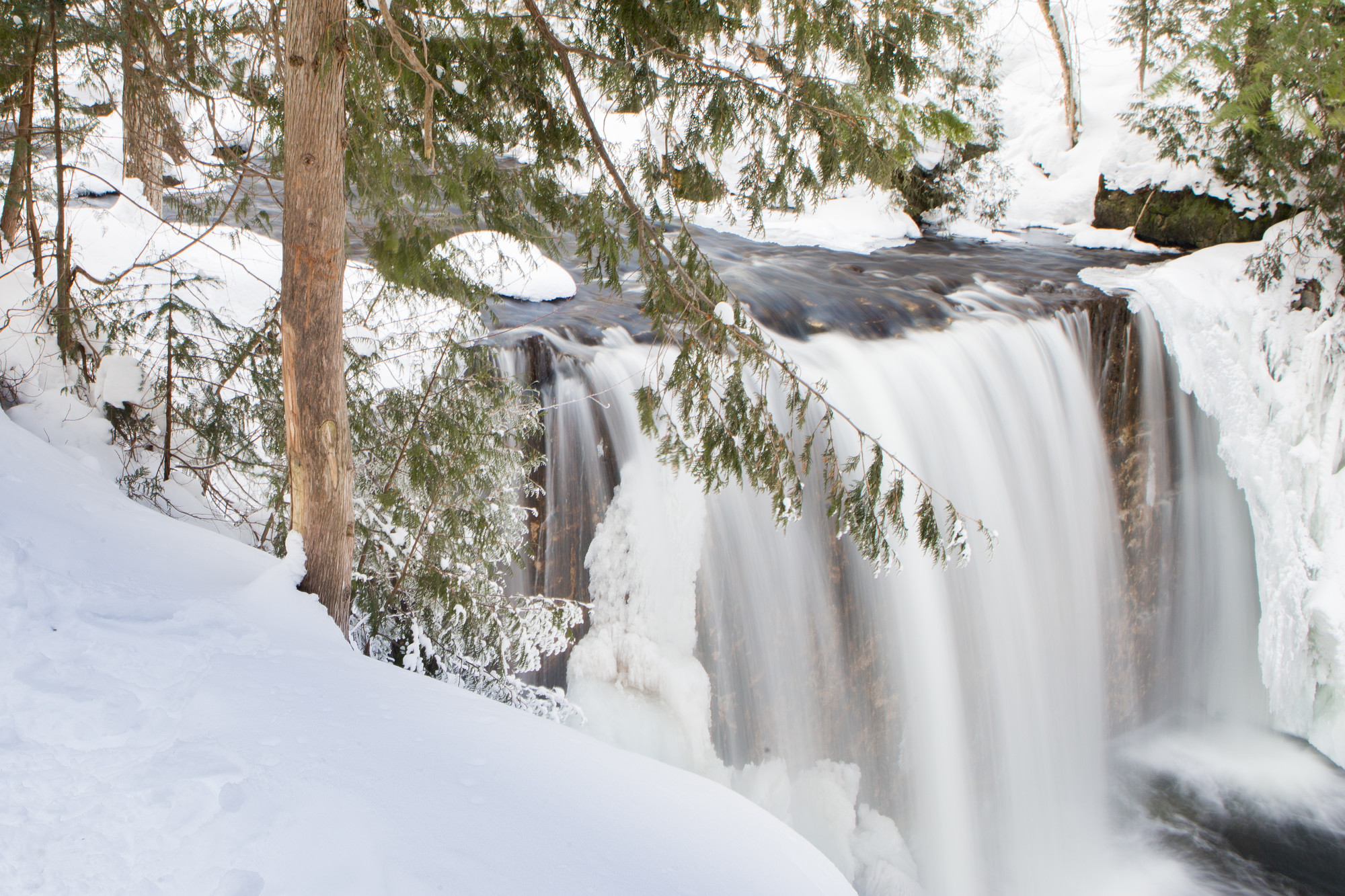 Water cascades down a waterfall in a wintry forest.