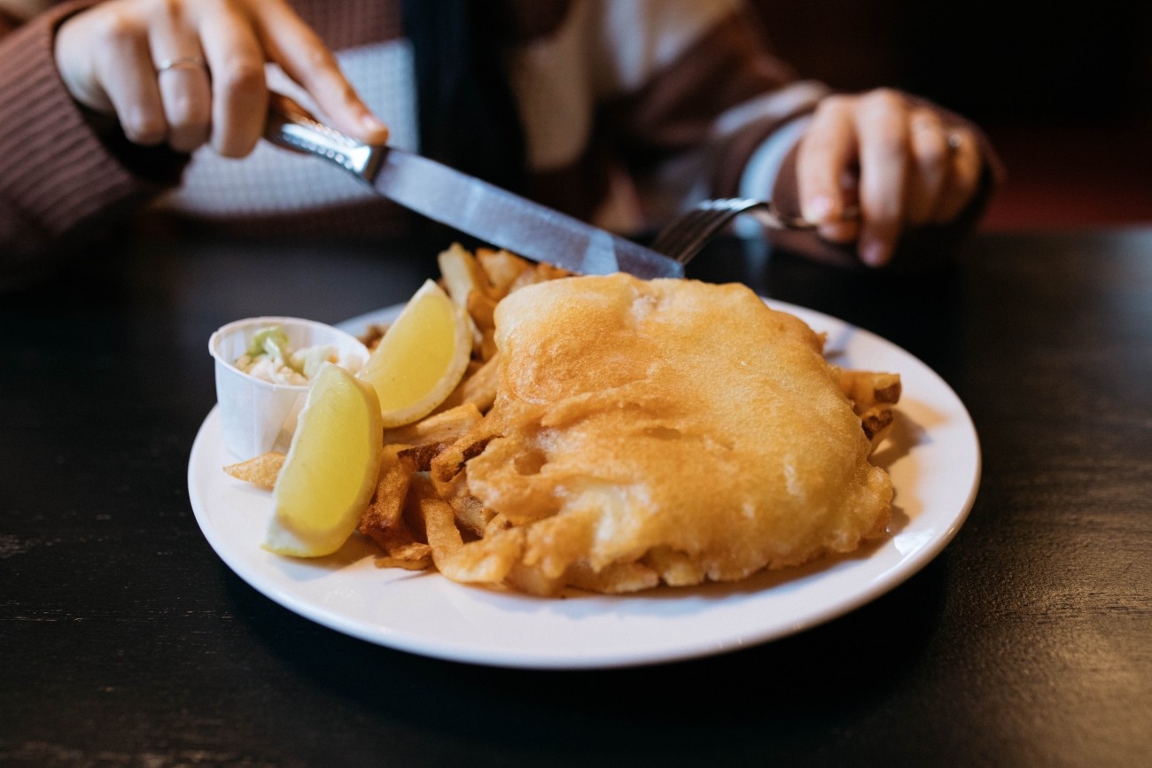 Close shot of a person cutting into a serving of battered fish.
