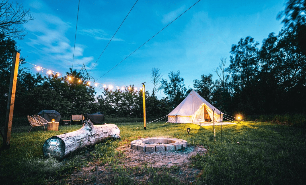 A campground with string lights, firepit and large tent.