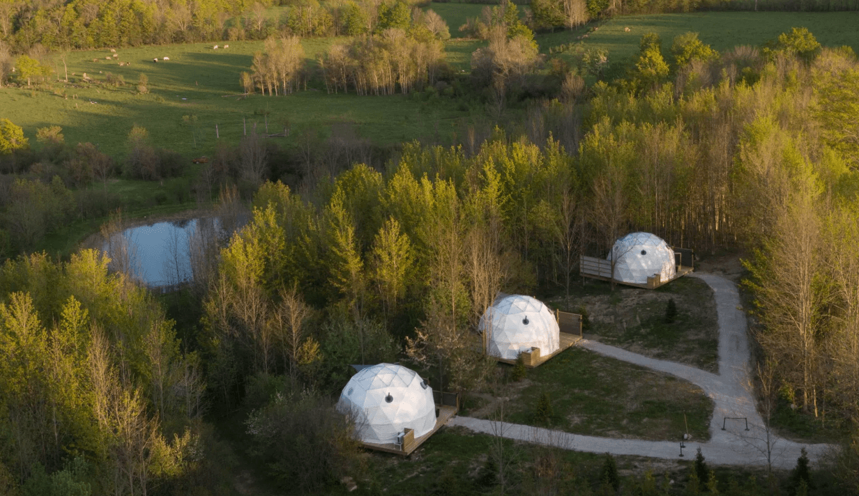 Aerial view of three geodesic camping domes in a wooded setting.