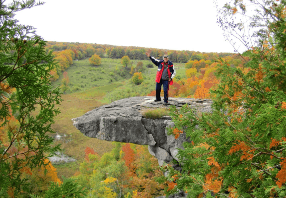 A person stands waving atop a rocky outcrop.