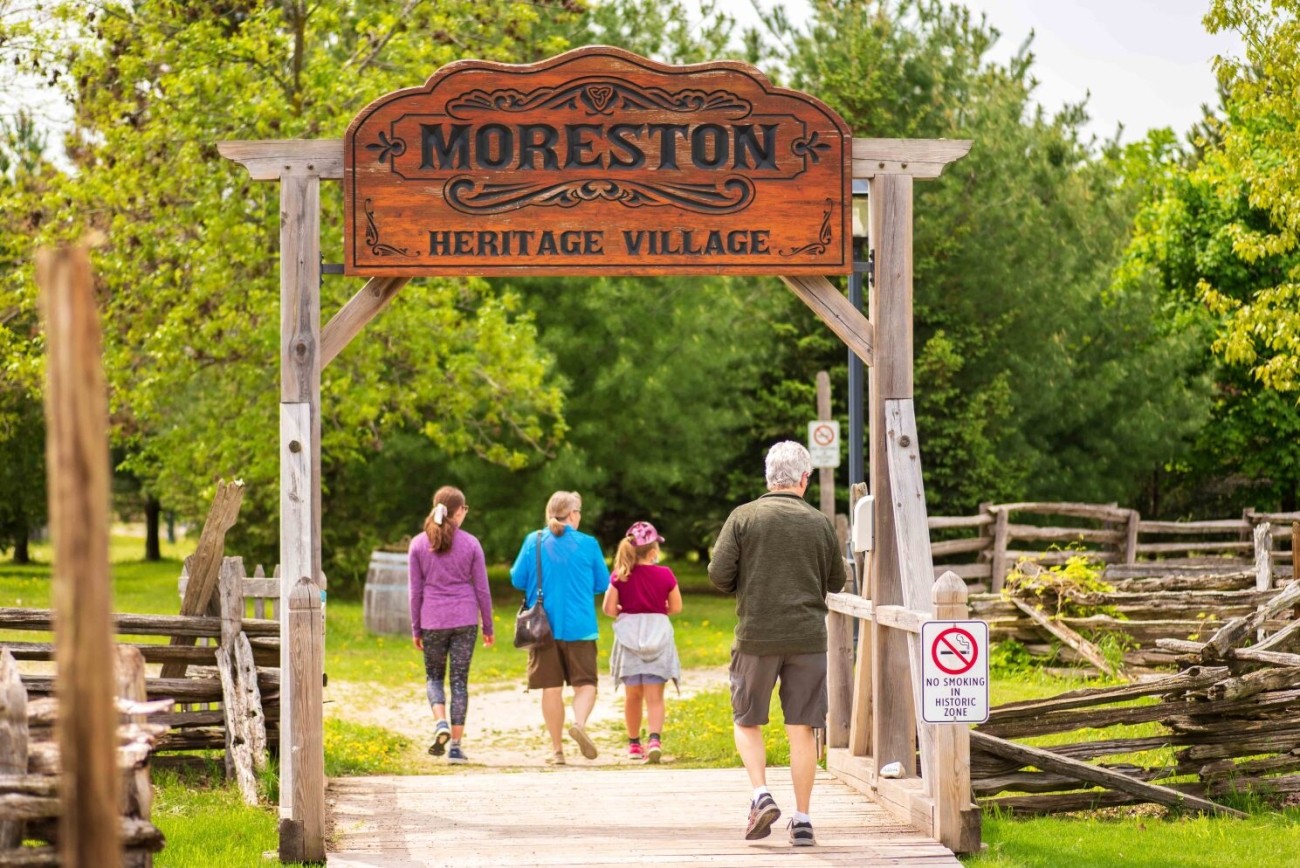 A family of four walks under a sign into Moreston Heritage Village.