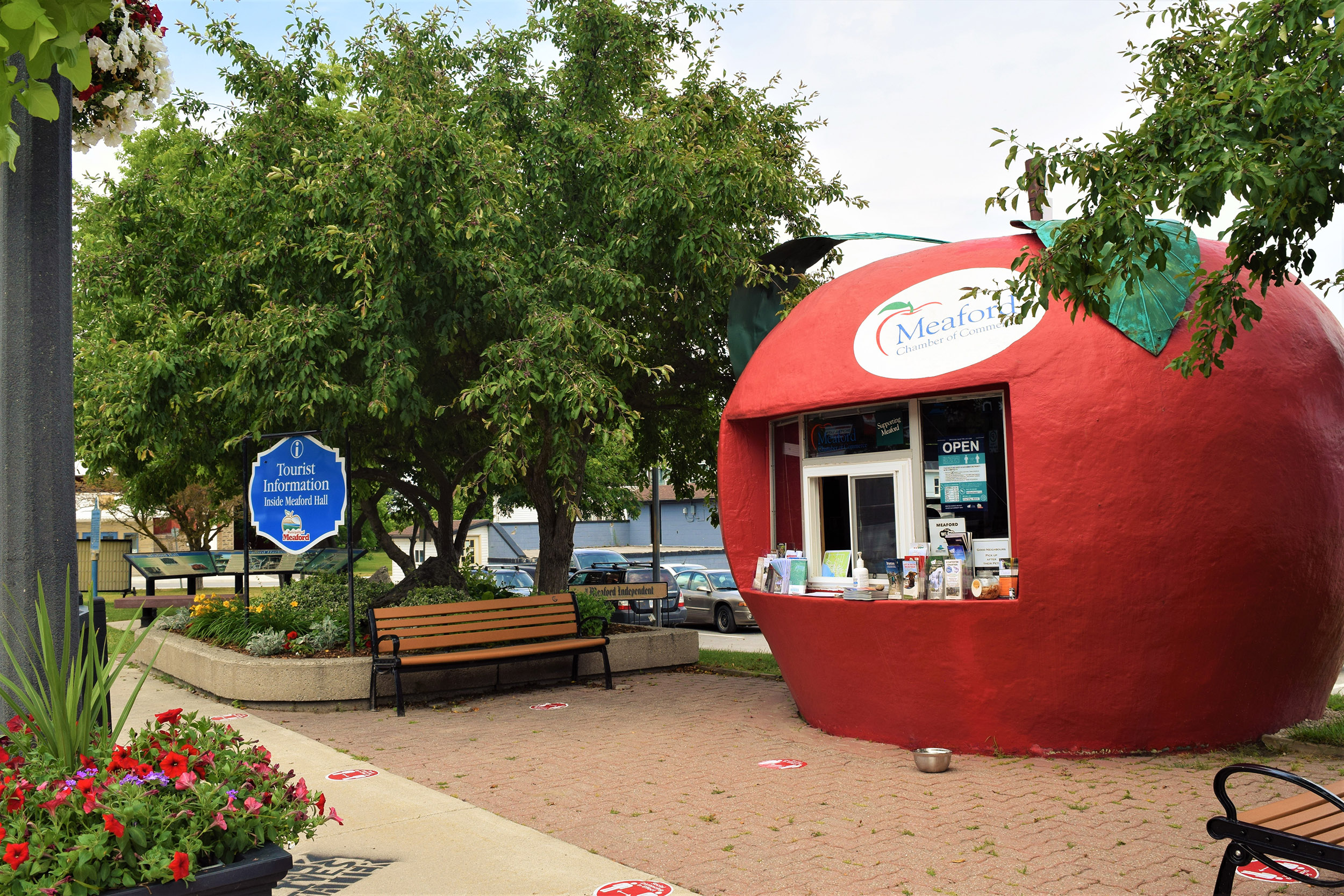 Tourist info booth shaped like a giant red apple beside trees and benches.