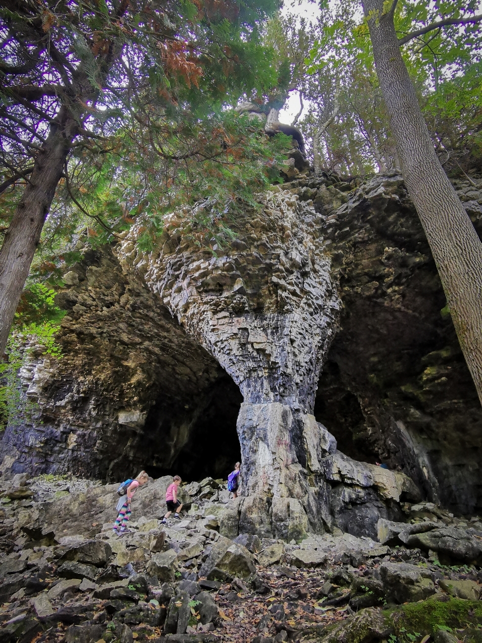 Dramatic view of three people hiking up rocky terrain into a large stone cave.