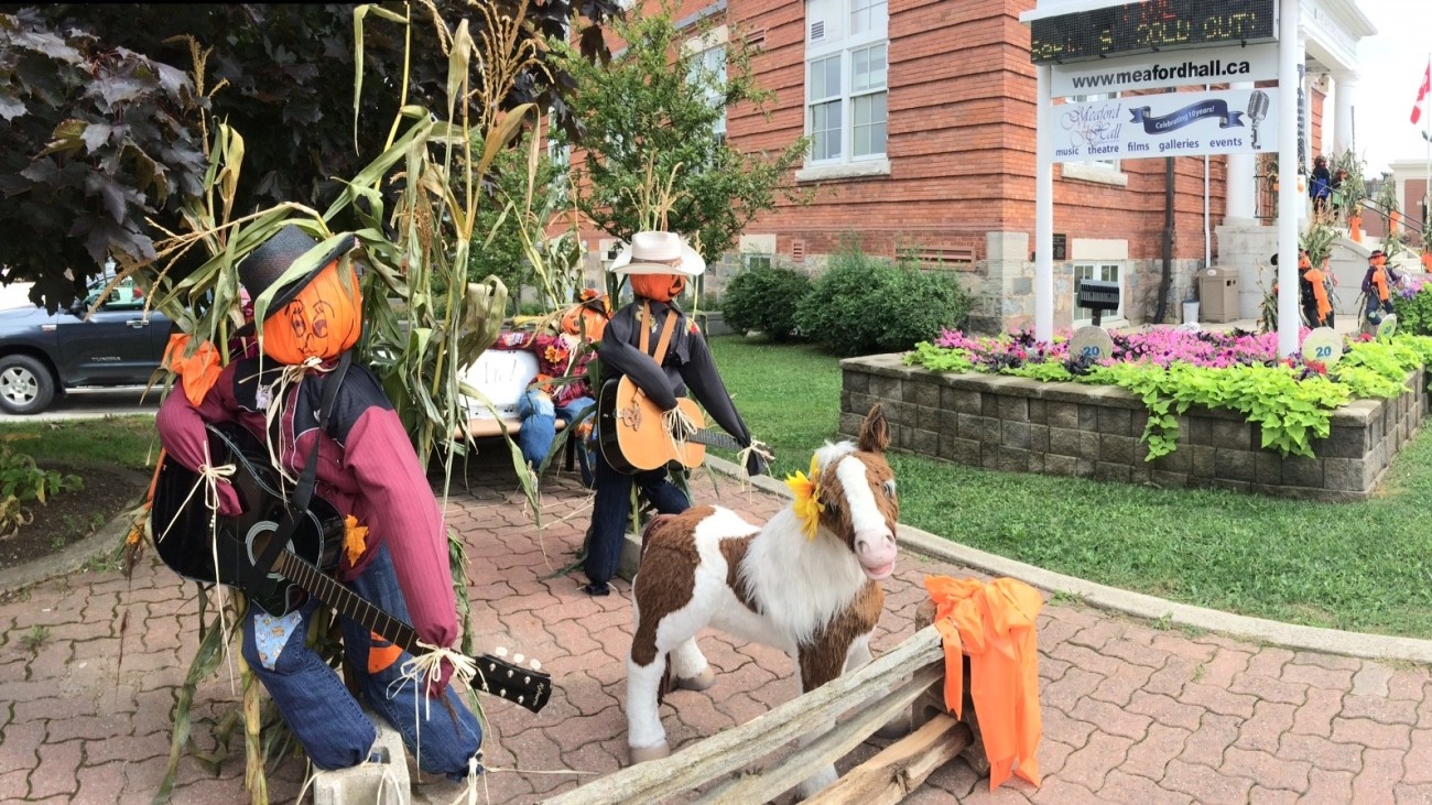Two scarecrows and a toy pony on a brick path.
