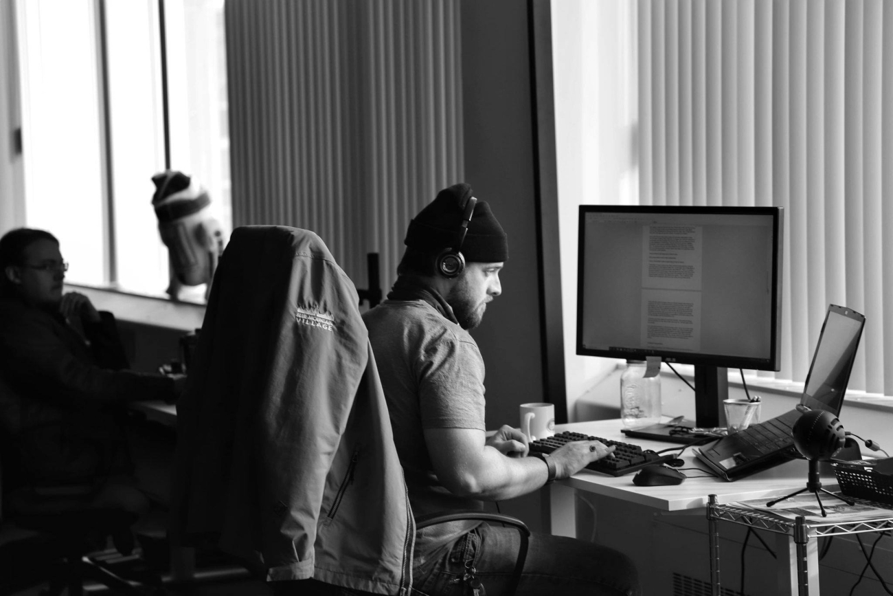 Black and white image of a man wearing headphones working on a computer in an office setting.