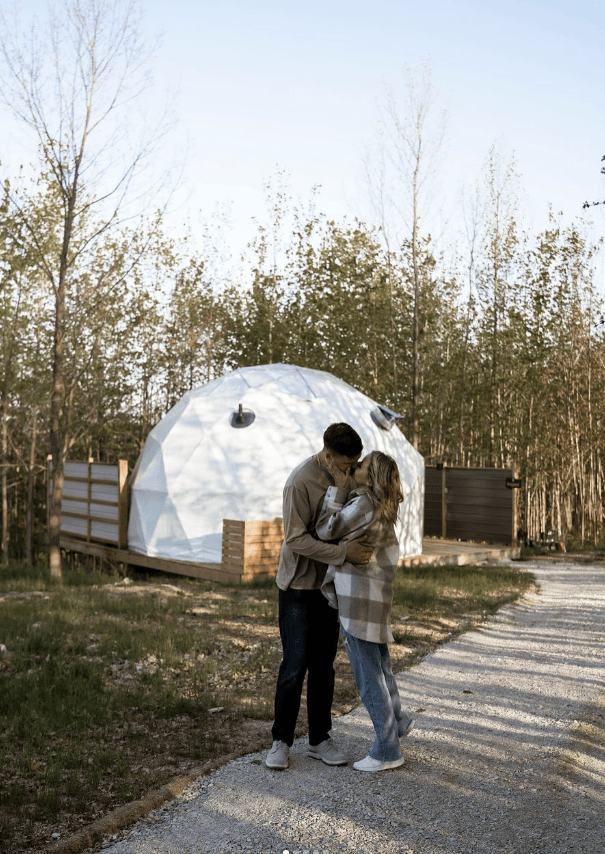 A couple kissing in front of a glamping dome